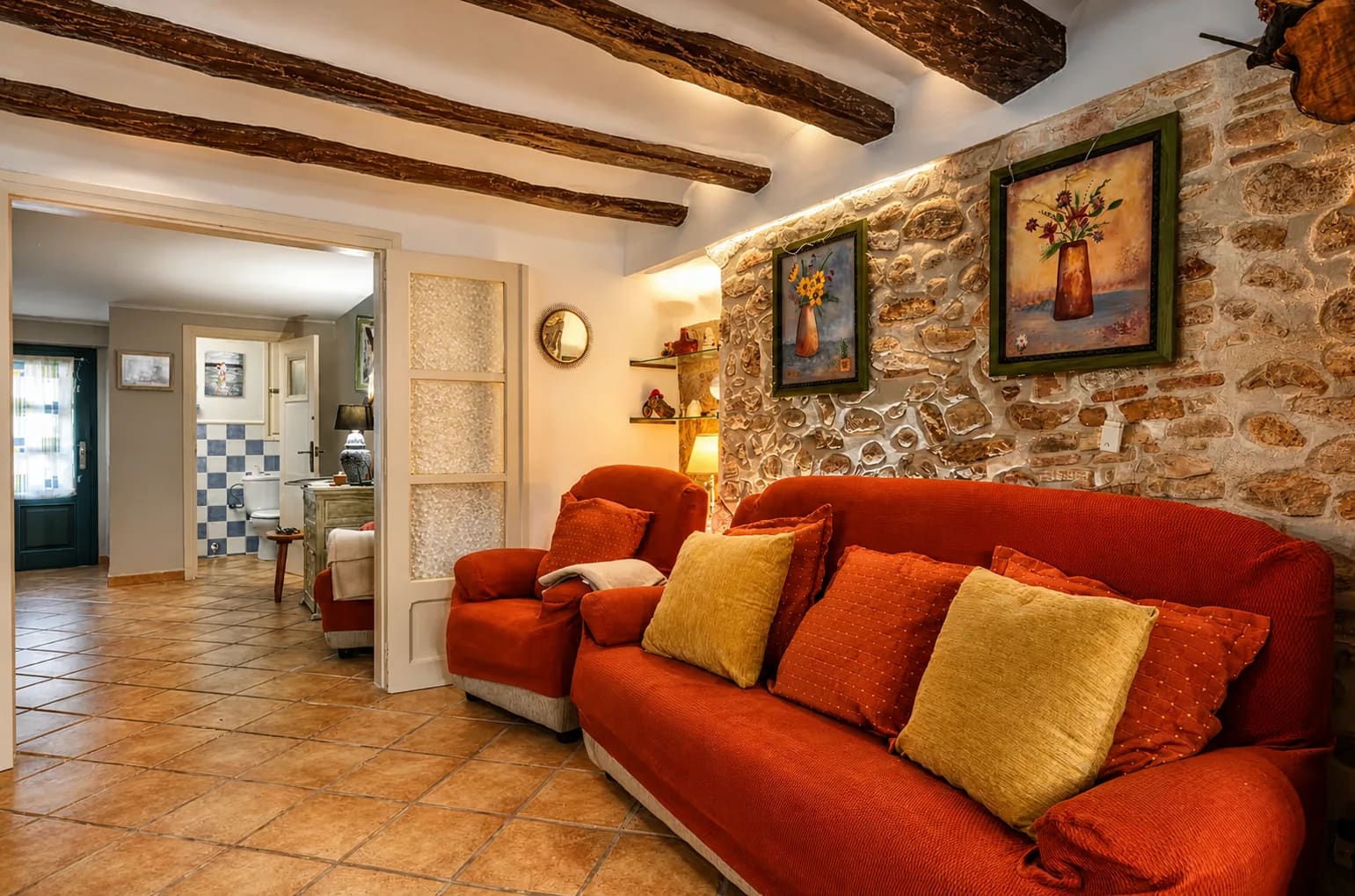 Rincón de la sala de estar con sofá y butaca rojos junto a la pared de piedra.