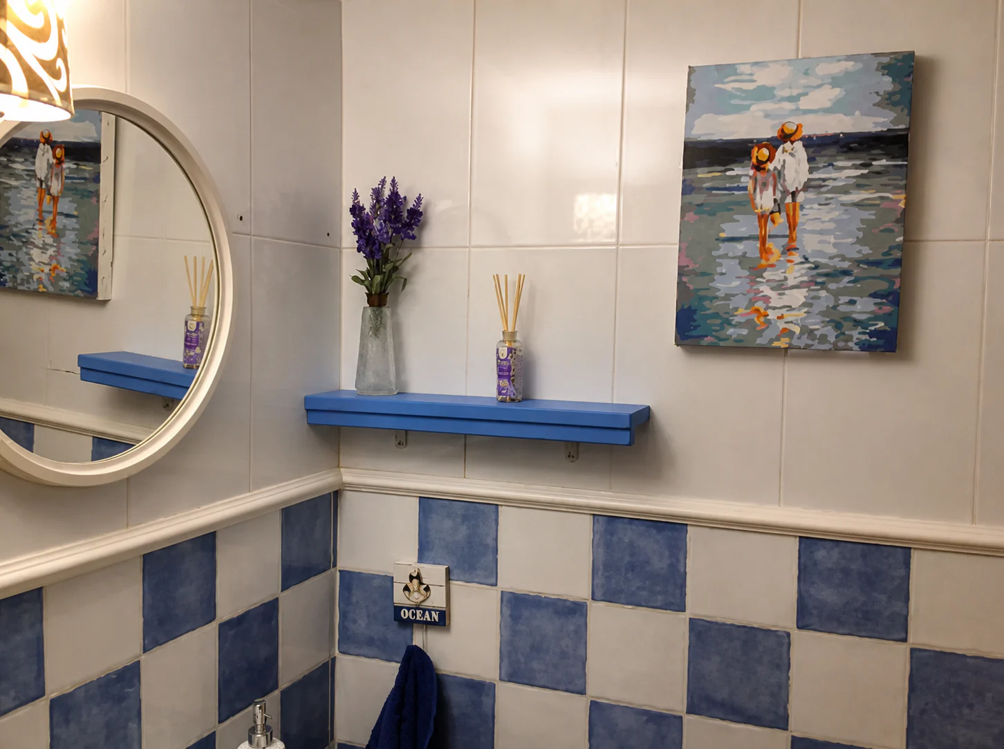 Aseo de la planta baja con azulejo azul y blanco, espejo redondo y un cuadro marino.