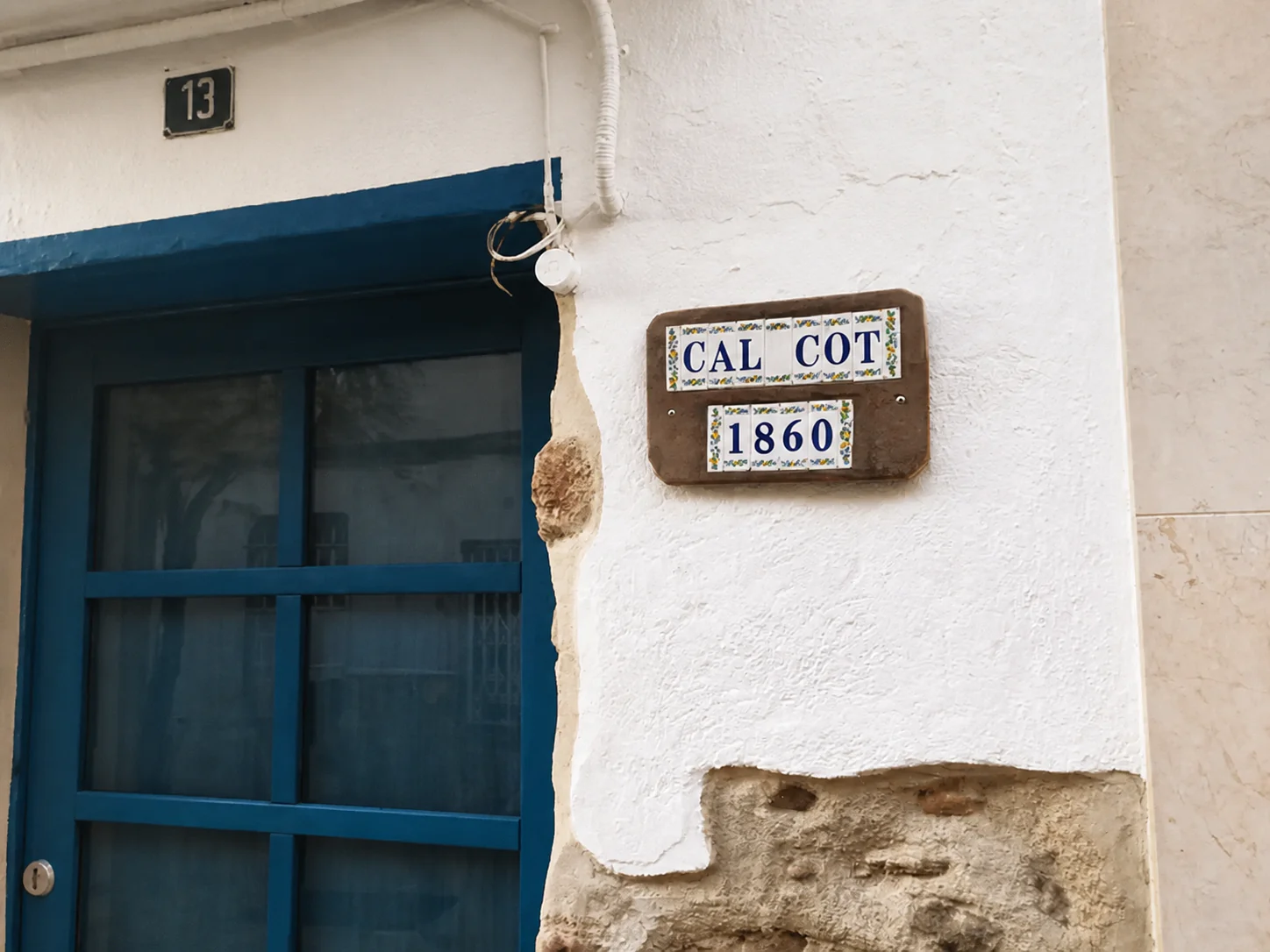 Puerta de entrada azul con la placa de azulejo «Cal Cot 1860» en la fachada.
