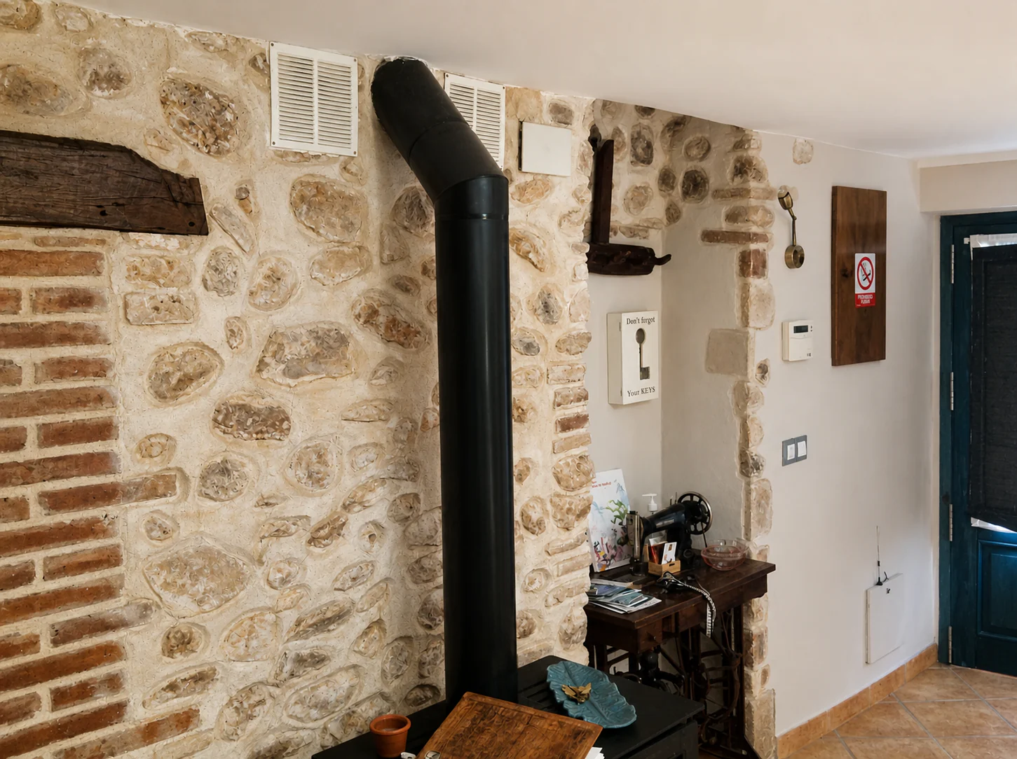 Recibidor con pared de piedra y ladrillo visto, estufa de leña y la puerta azul al fondo.
